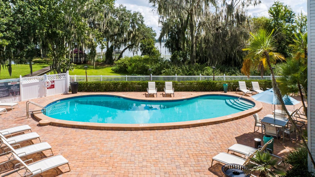 A pool surrounded by a brick patio and lounge chairs.