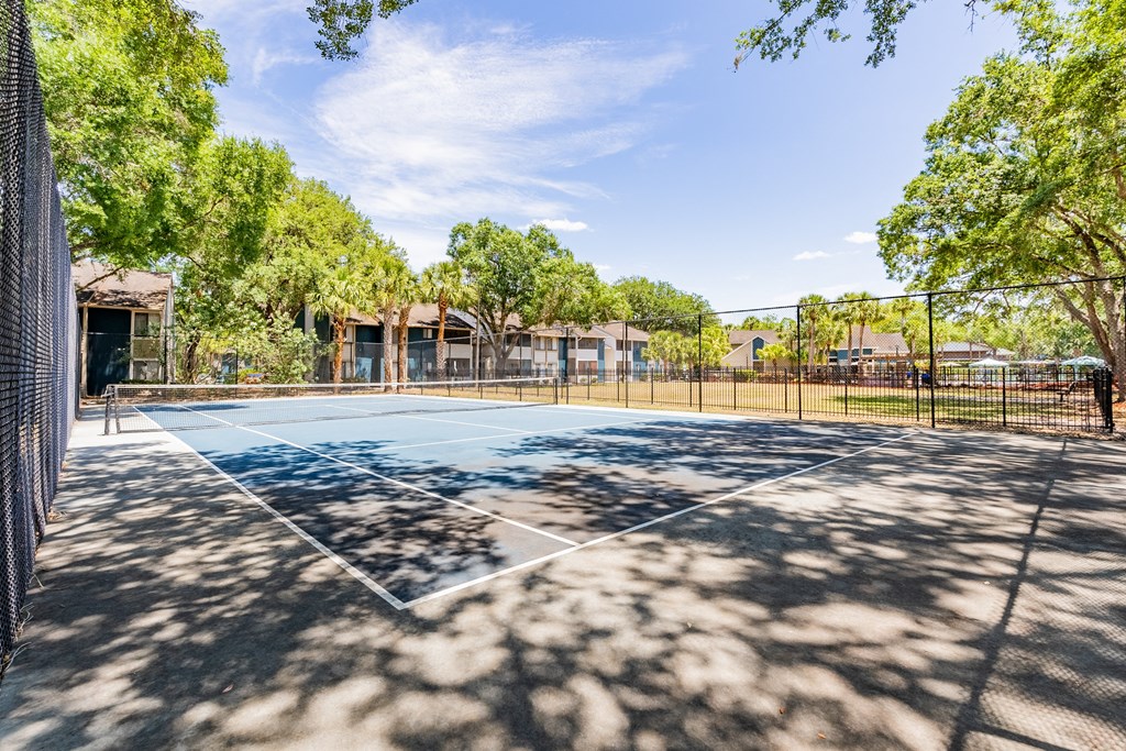 a tennis court with trees and a fence around it  at Fisherman's Landing Apartment Homes, Tampa, Florida