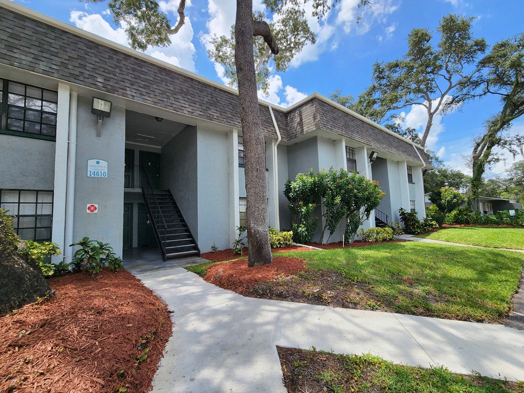 the front of a white building with a sidewalk and trees at Greenwich Commons Apartment Homes, Tampa, FL