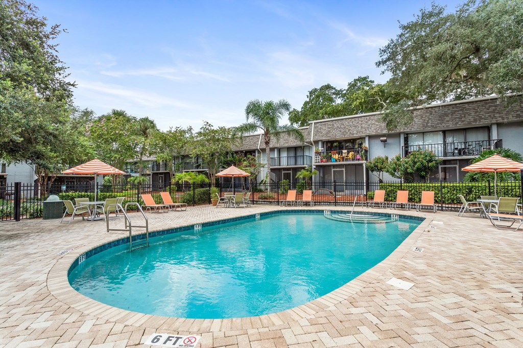 a resort style pool with chairs and umbrellas in front of a building a resort style pool with chairs and umbrellas in front of a building at Greenwich Commons Apartment Homes, Tampa, 33613