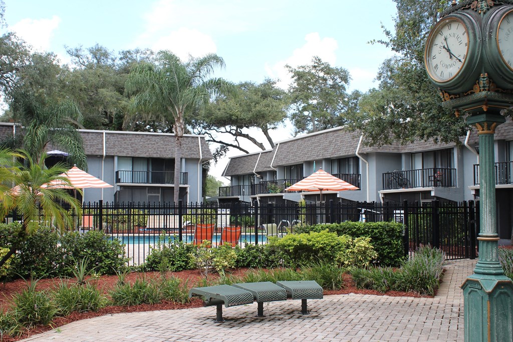 a large clock sitting in front of a pool with umbrellas at Greenwich Commons Apartment Homes, Tampa, 33613