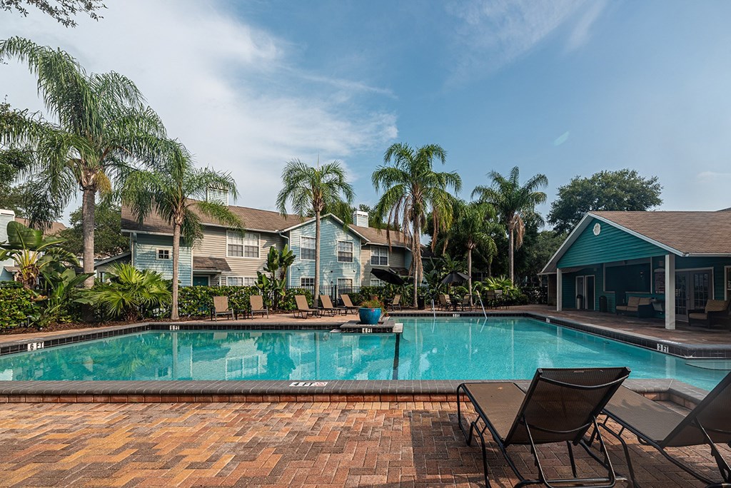 a swimming pool with chairs and palm trees in front of a house at Madison Oaks Apartment Homes, LLC, Palm Harbor, 34684