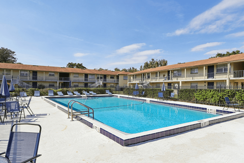 A swimming pool surrounded by lounge chairs and umbrellas in front of a building.
