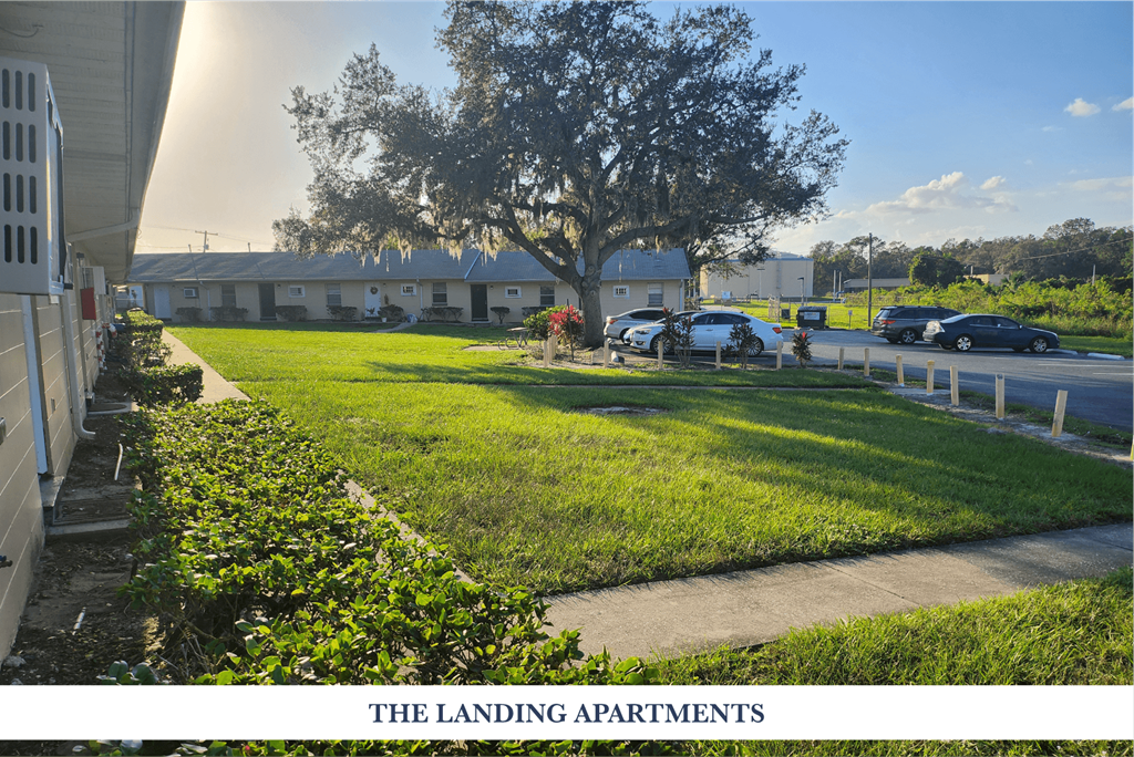 A view of THE LANDING APARTMENTS with a tree and cars parked in the background.