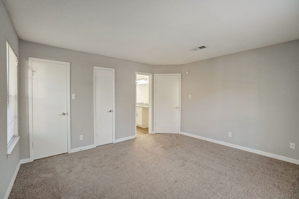 A room with carpeted floor and white walls with four doors.
