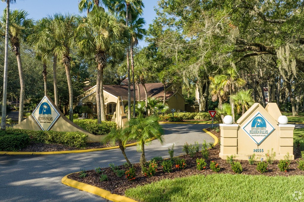 A sign for a community named "Waterfall Estates" is displayed in front of a well-manicured lawn and palm trees.