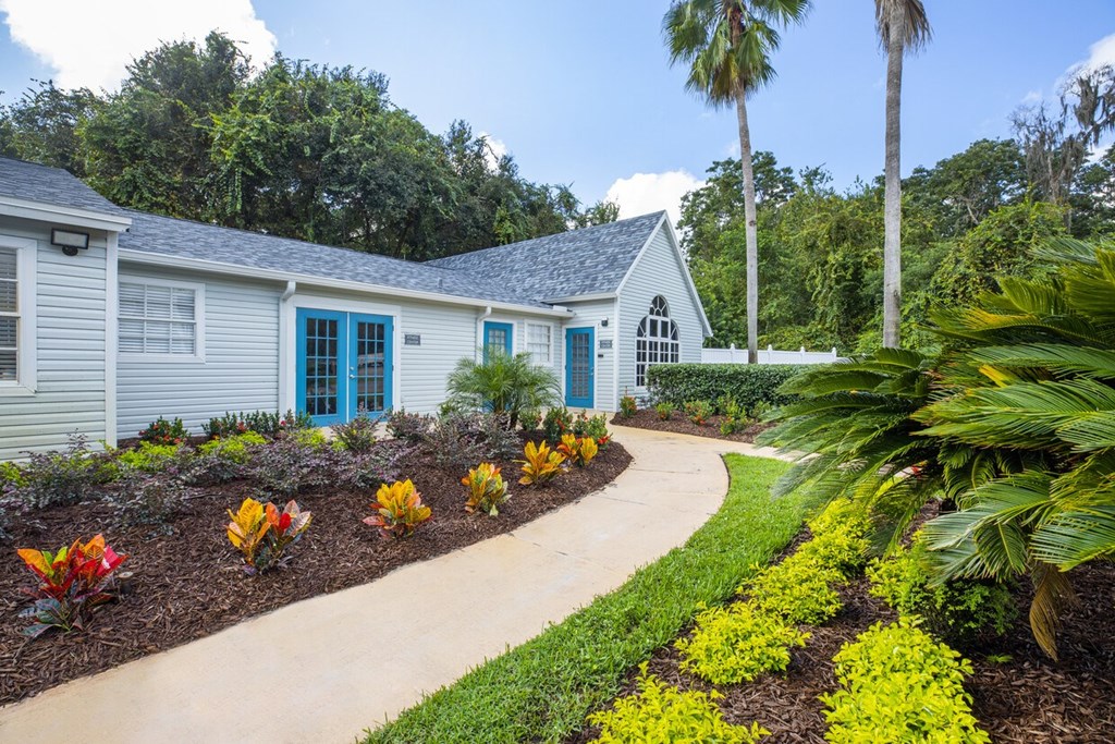 A small house with a blue door is surrounded by a garden with yellow flowers.