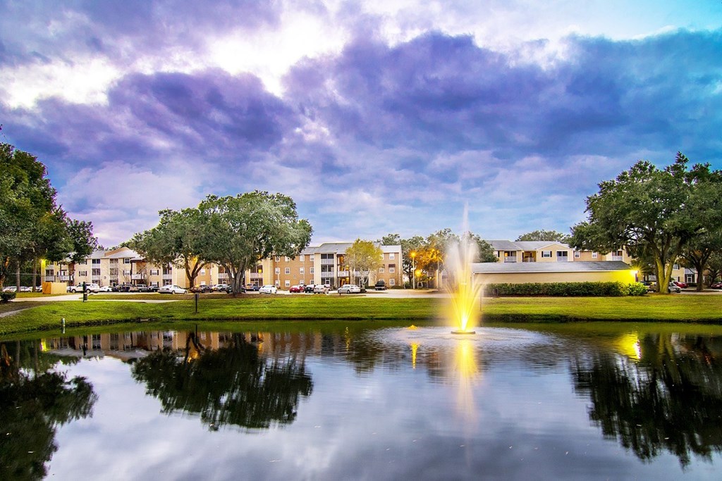 A fountain in the middle of a pond in front of a building.