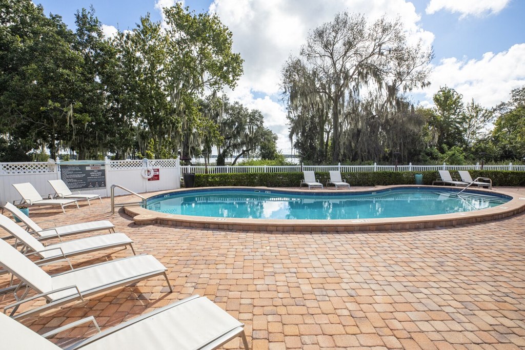 A pool surrounded by trees and chairs.