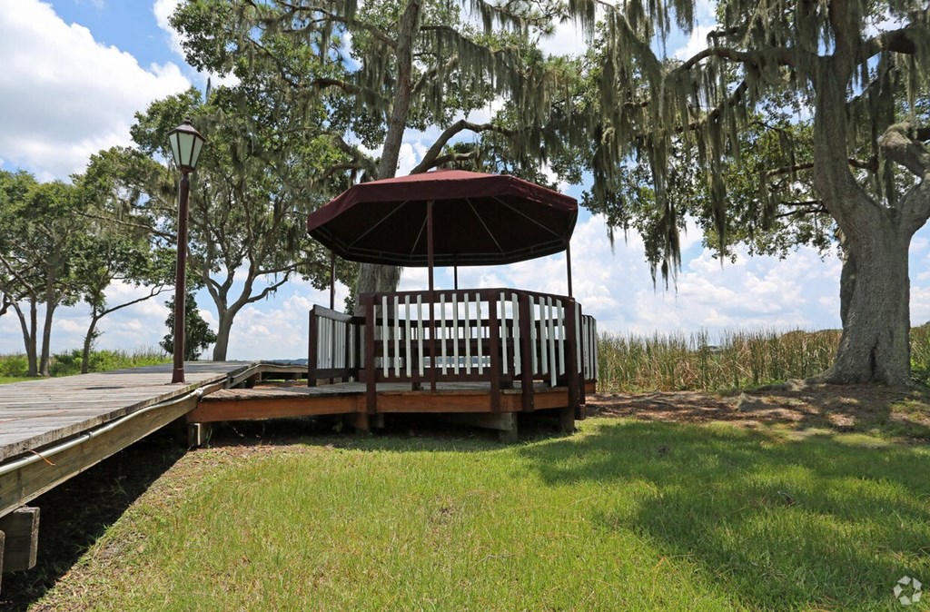 A gazebo with a red roof is surrounded by green grass and trees.
