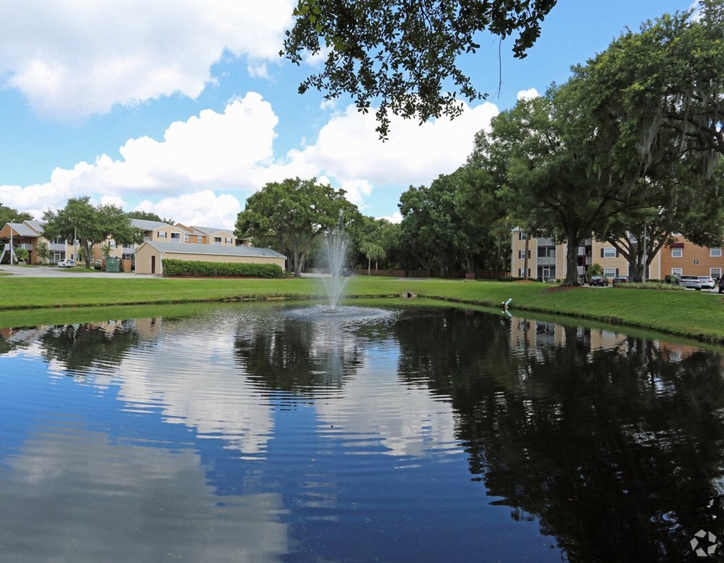 A fountain in the middle of a pond surrounded by trees and buildings.