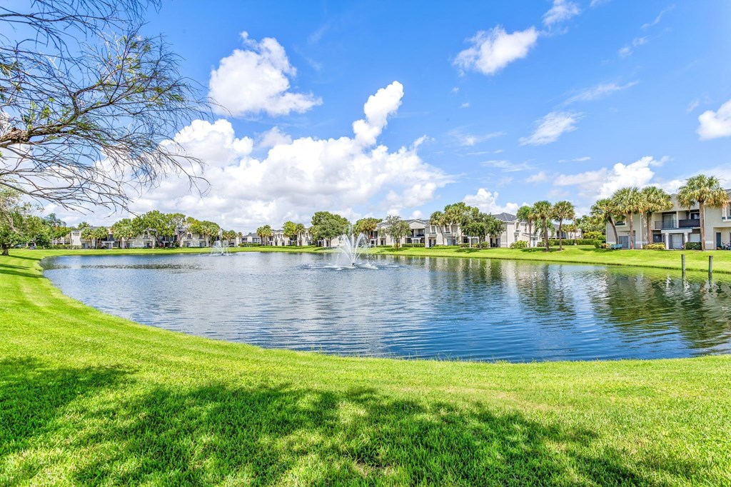 a lake with a fountain in the middle of a grassy field at Waterford Park Apartment Homes, LLC, Lauderhill Florida