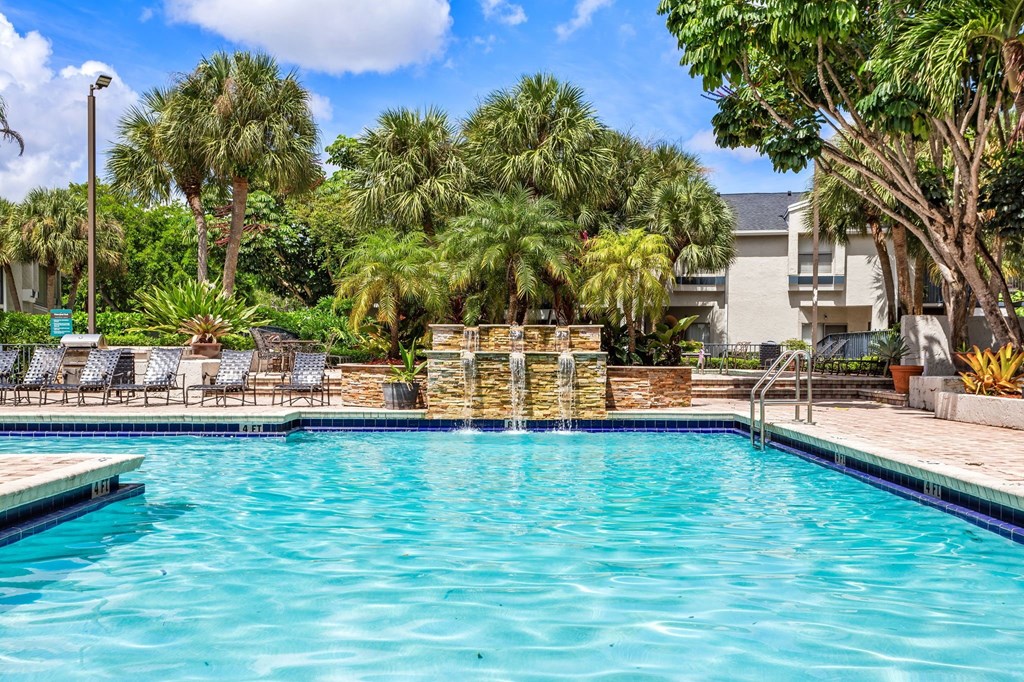 a swimming pool with palm trees and a building in the background at Waterford Park Apartment Homes, LLC, Lauderhill, FL