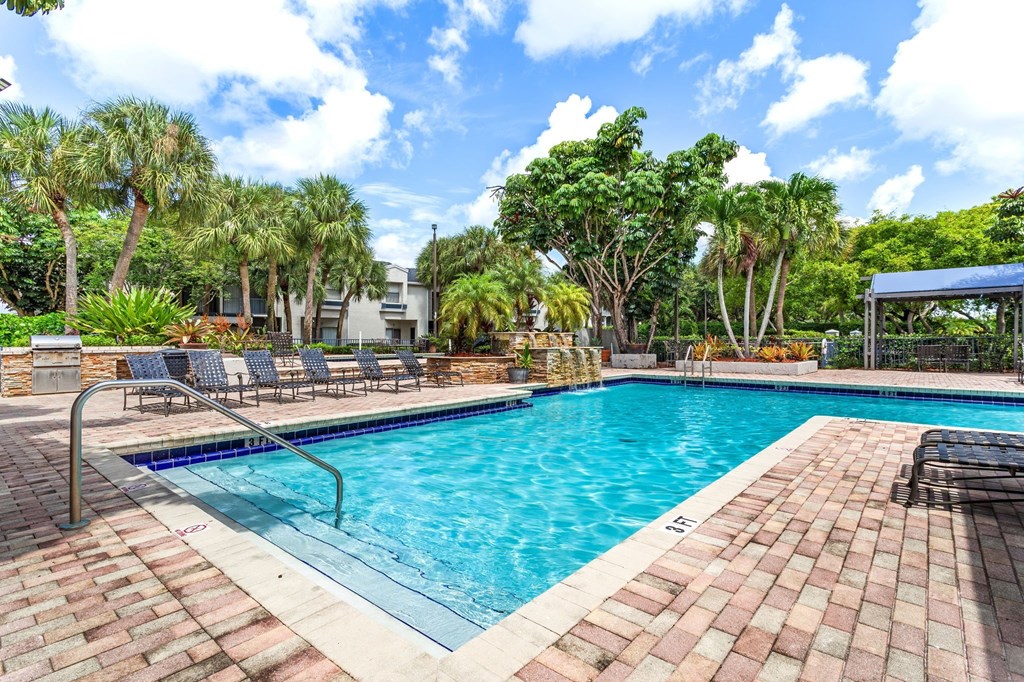 a swimming pool with trees and chairs around it at Waterford Park Apartment Homes, LLC, Lauderhill, FL 33319