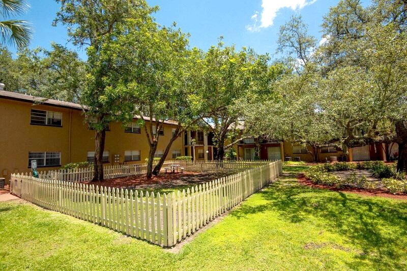 a yard with a fence and trees in front of a yellow house  at Oak Manor Apartment Homes, Tampa