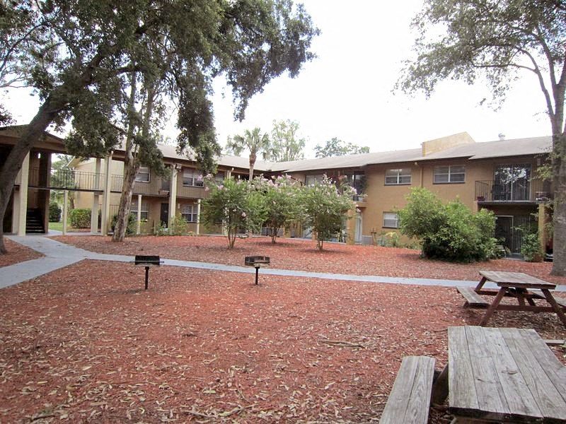a courtyard with picnic tables and benches in front of an apartment building  at Oak Manor Apartment Homes, Tampa, FL, 33617