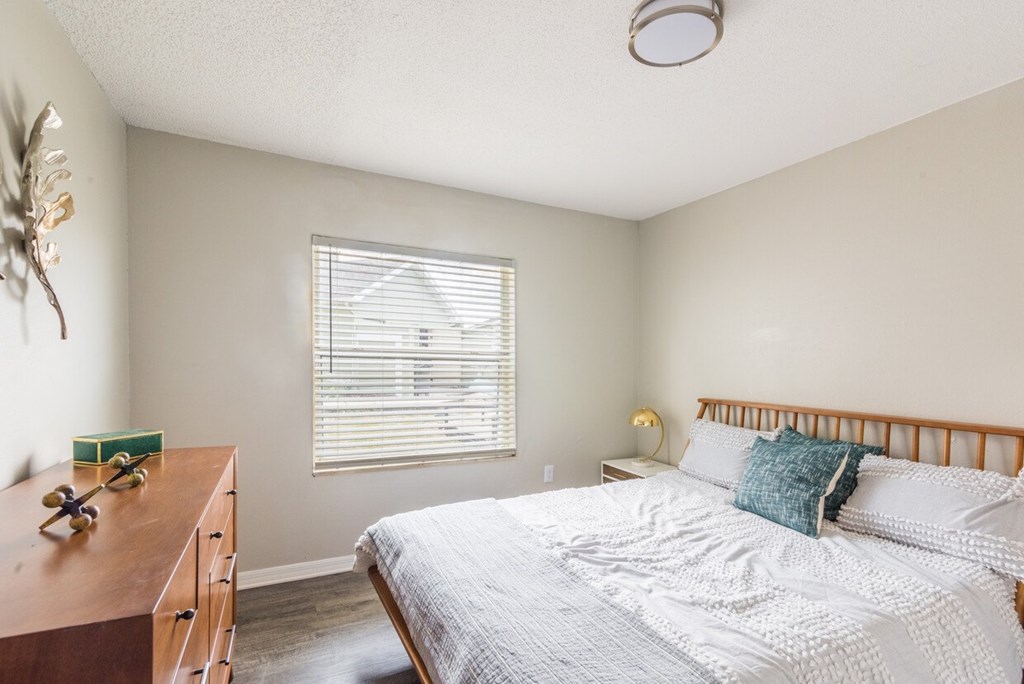 A bedroom with a bed, nightstand, and window with blinds.