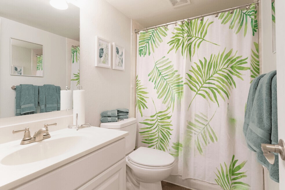 A bathroom with white countertop and cabinets, sterling fixtures, and wooden flooring.
