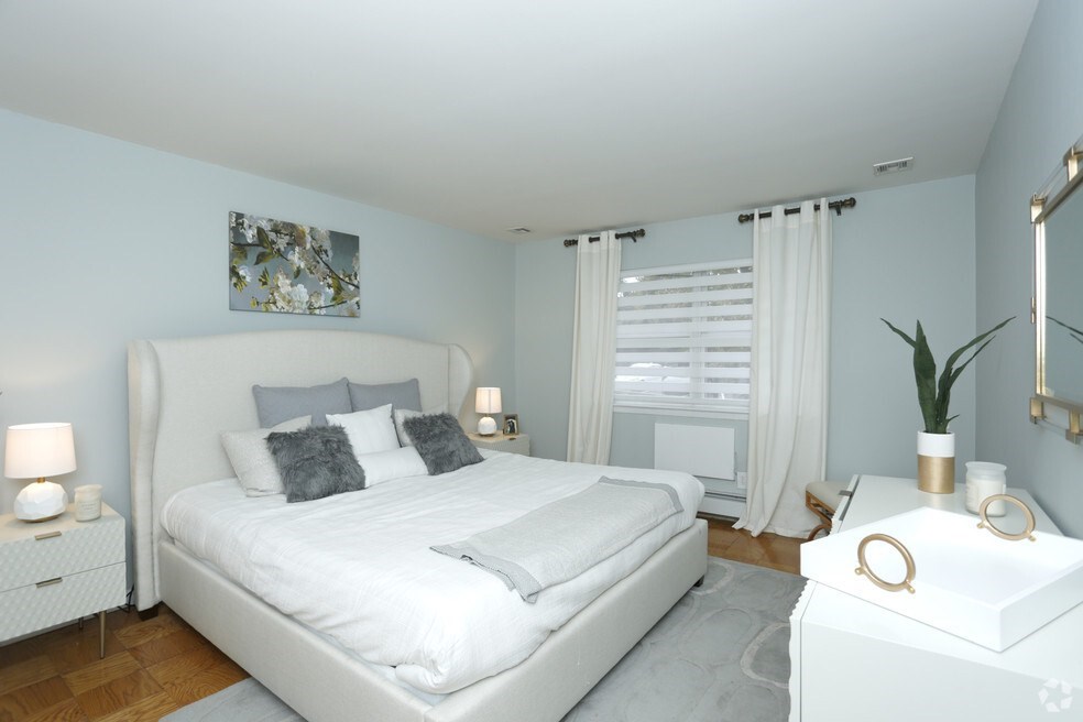 A white bedroom with a large bed and a nightstand with a plant on it.