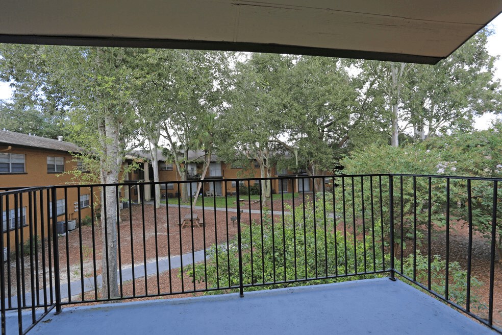 A spacious balcony or patio with a courtyard view of green space and seating areas. Railed and covered  Balcony