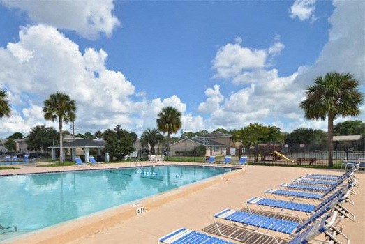 A pool with blue lounge chairs and palm trees in the background.