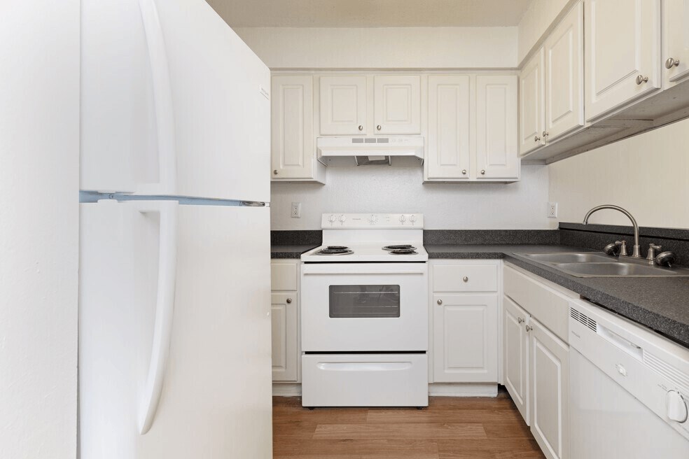 A spacious kitchen with white round inset cabinets, dark contrasting counter tops, matching white stove, refrigerator, and dishwasher
