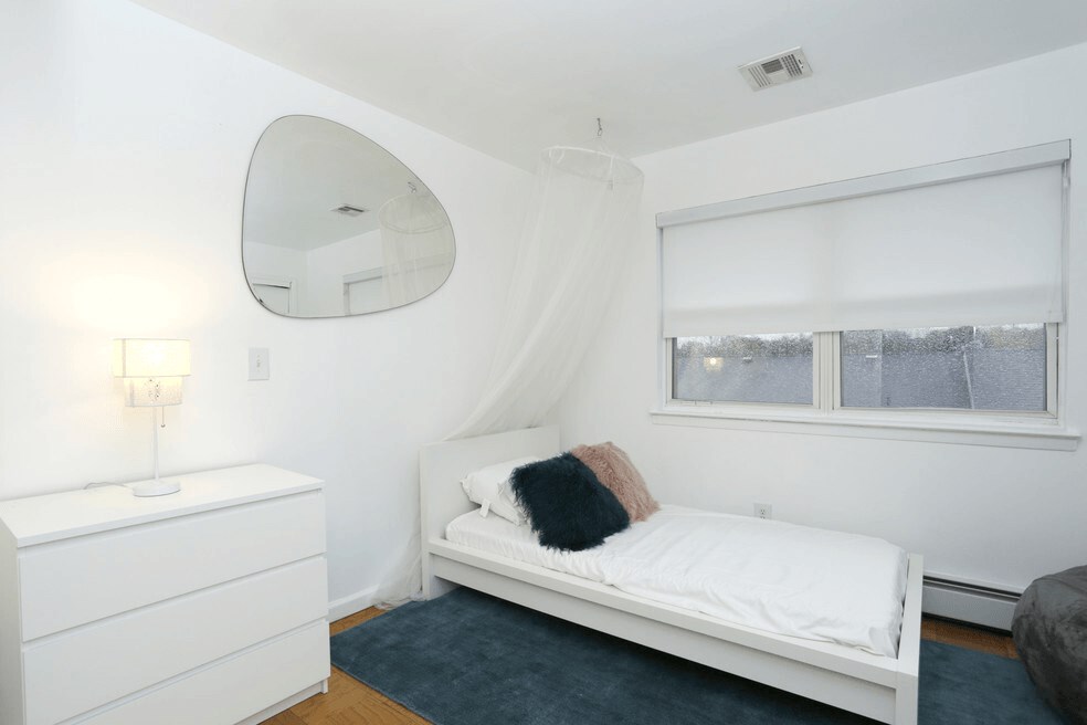 A white bedroom with a bed, dresser, and mirror.