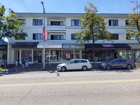 A white car is parked in front of a building with a purple awning.