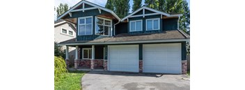 A two-story house with a green roof and white garage doors.
