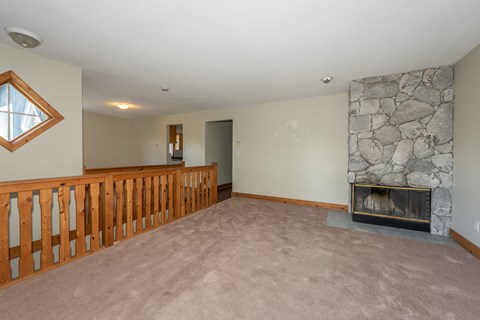 A living room with a stone fireplace and a wooden railing.