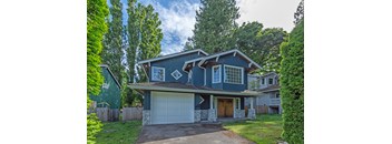 A blue house with a white garage door is surrounded by greenery.