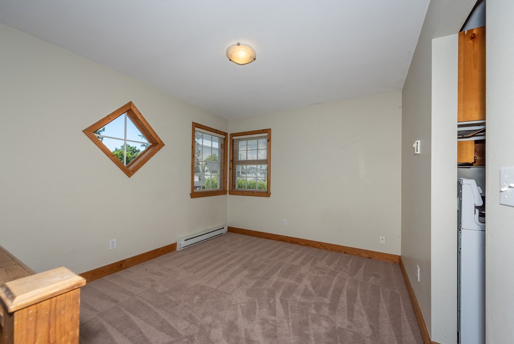 an empty living room with two windows and a kitchenette