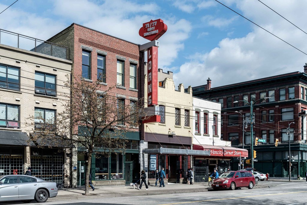 a view of a street corner with people walking and cars parked on the side of the road