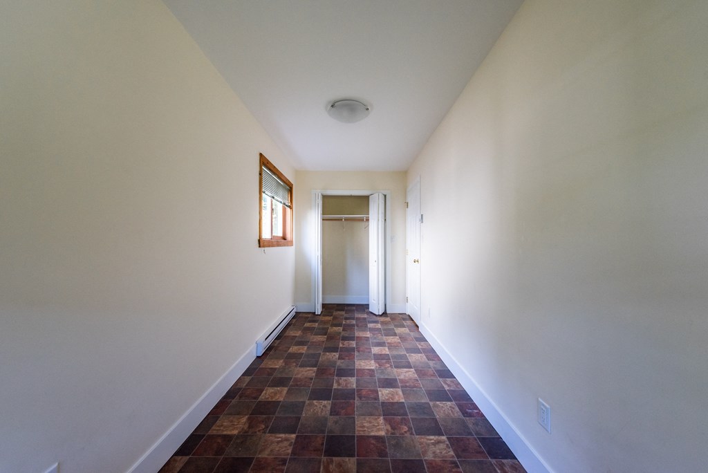 a corridor in a house with white walls and a brown tile floor