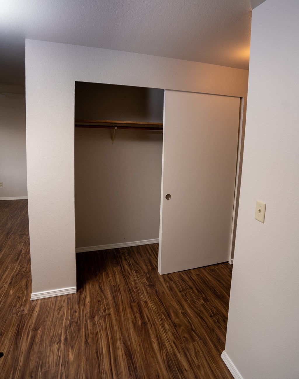 an open door leads into a bedroom with a closet and hardwood floors