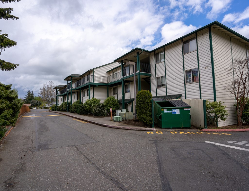 a row of apartment buildings with a green recycling bin in front of them
