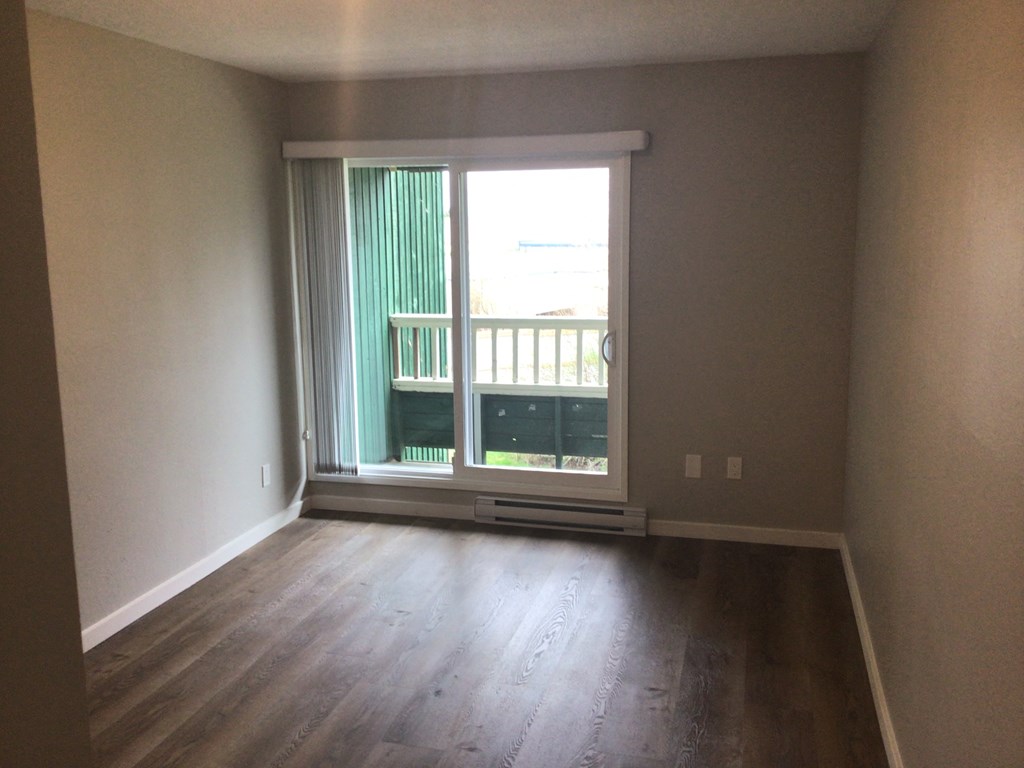 an empty living room with a large window and wooden floors