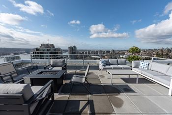 a rooftop terrace with couches and tables and a city in the background