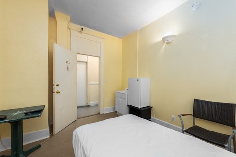 a bedroom with a bed and a fridge and a chair