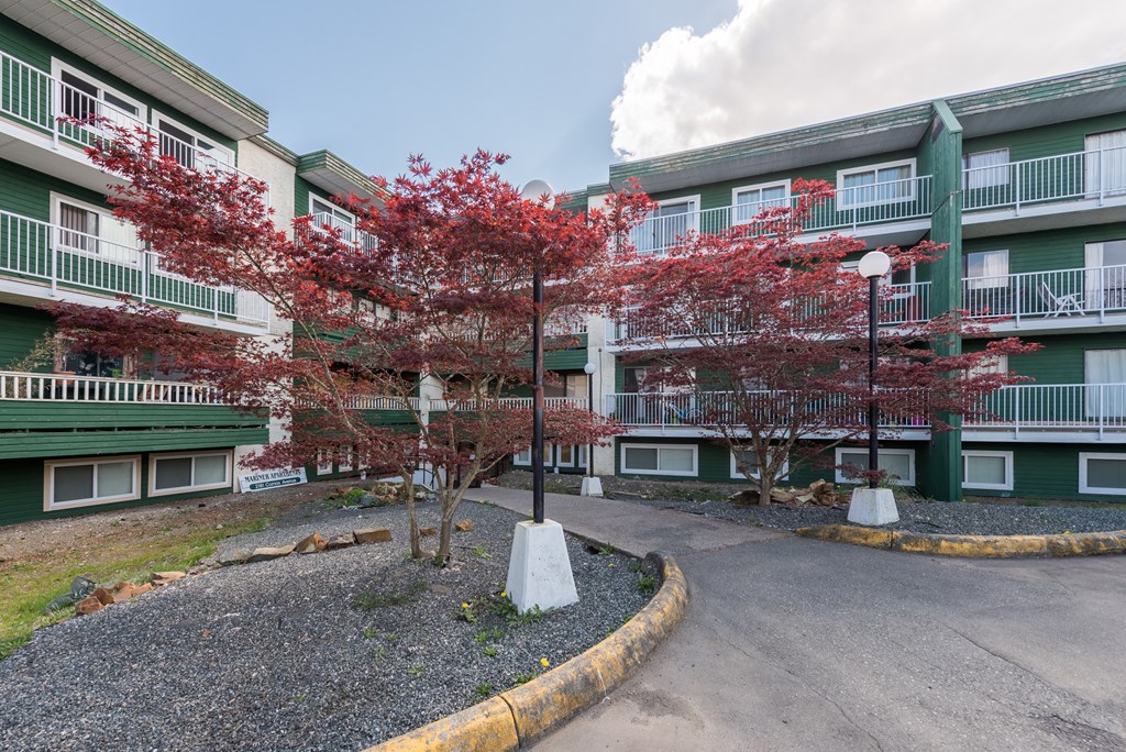 a view of the entrance to a green apartment building with red trees in front of it