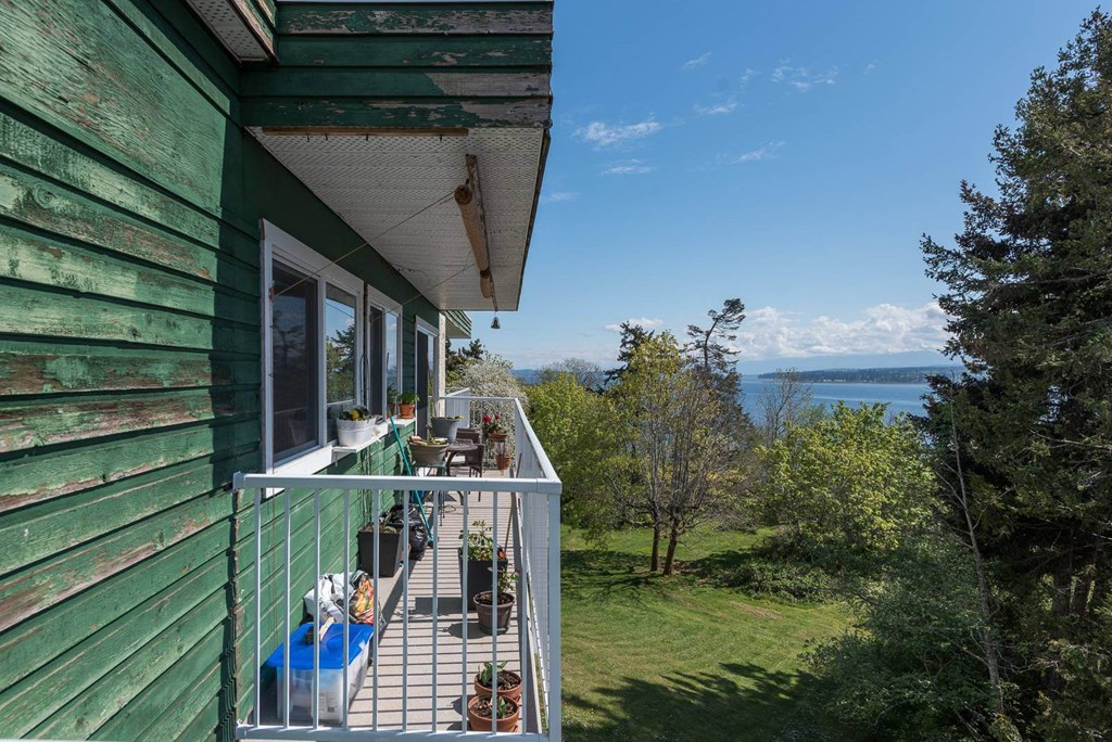 A green house with a balcony overlooking a grassy area and a body of water.