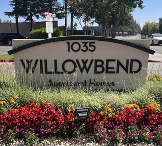 a sign for willowbend with flowers in front of it