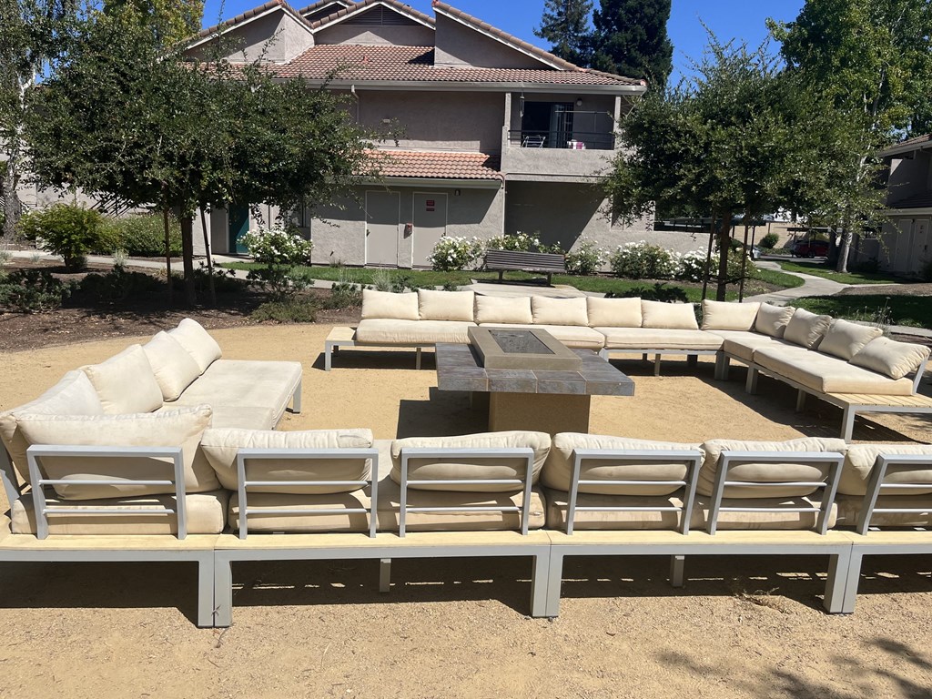 a patio with white couches and a fire pit in front of a house