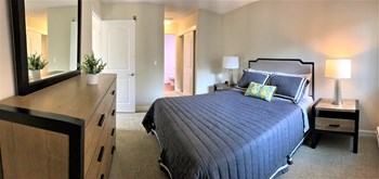 one bedroom model with queen size bed, drawers, side tables. short hallway closet walkway to bathroom - Photo Gallery 3