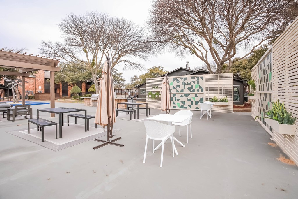 A patio with white chairs and a table with a brown umbrella.