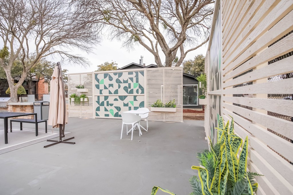 A patio with a table and chairs and a wall with a green and white mosaic.