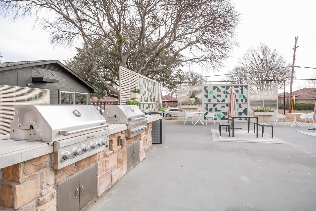 A patio with a grill and chairs is surrounded by a brick wall.