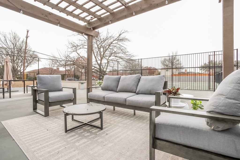 A patio with grey couches and a wooden pergola.