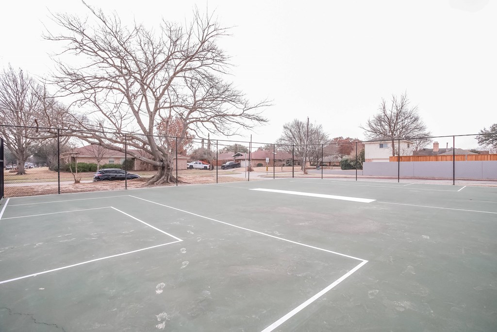 A tennis court with a car and trees in the background.