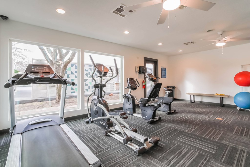 A gym with a treadmill, elliptical machines, and exercise balls.